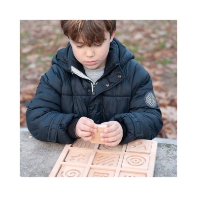 Criança com casaco azul joga jogo de tabuleiro de madeira com peças gravadas ao ar livre