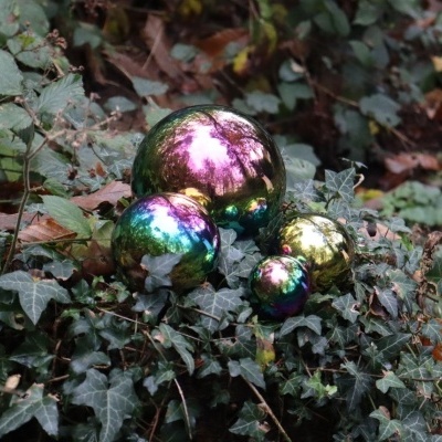 Três esferas decorativas iridescentes sobre folhas verdes