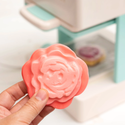 Brinquedo em forma de flor cor-de-rosa segurado à frente de máquina de cozinha infantil branca e azul