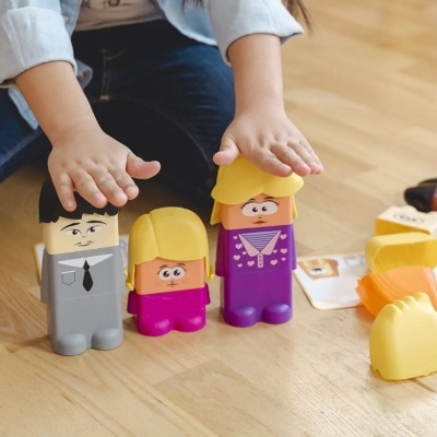 Bonecos de blocos de construção coloridos numa superfície de madeira com mãos de criança a tocar