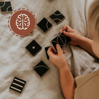 Blocos geométricos de madeira pretos com padrões brancos nas mãos de uma criança sobre tecido bege