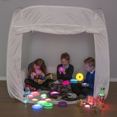 Três crianças brincando dentro de tenda branca com vários brinquedos e luzes coloridas