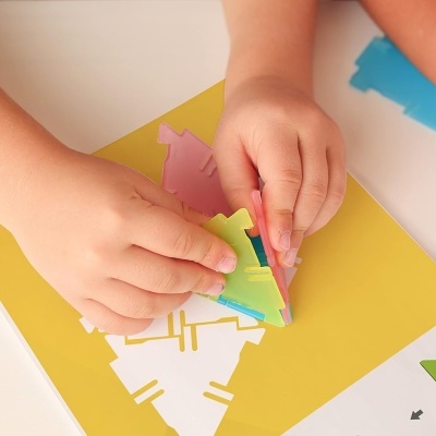 Mãos de crianças a montar puzzle tangram colorido sobre base amarela e papel com desenhos