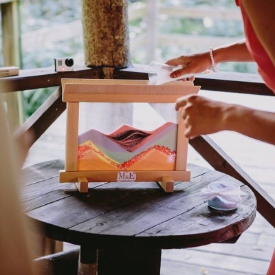 Relógio de areia de madeira com areias coloridas em camadas em mesa redonda de madeira.