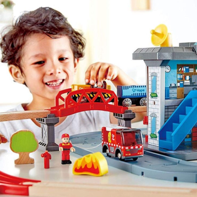 Criança a brincar com brinquedo de madeira de camião de bombeiros e ponte.