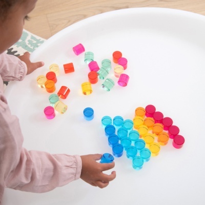 Criança a manusear pequenos copos de plástico coloridos numa bandeja branca