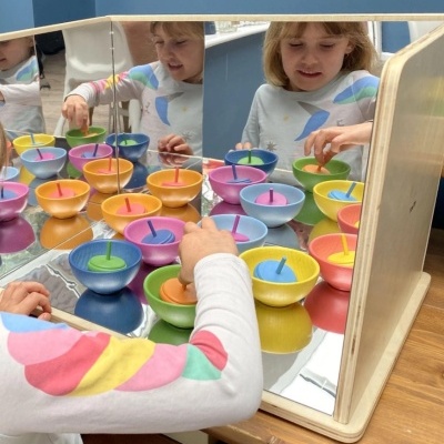 Mesa com copos coloridos empilhados e criança a brincar, refletidos num espelho
