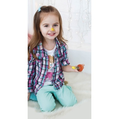 Menina com camisa xadrez e calças verdes a pintar sentado numa superfície branca