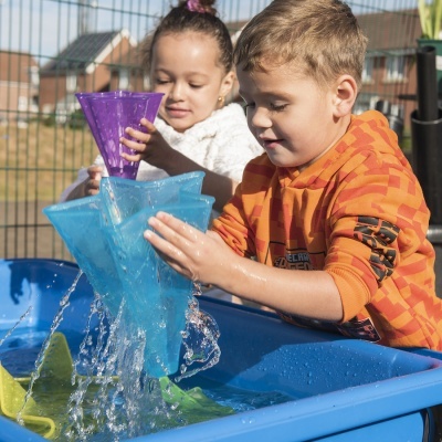 Crianças a brincar com água usando brinquedos coloridos numa mesa azul