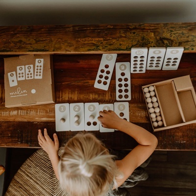 Jogo educativo de madeira com peças numeradas e bolas, criança a brincar numa mesa de madeira.