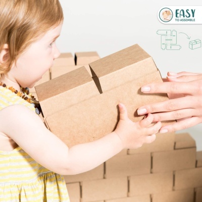 Menina com vestido amarelo segurando bloco de construção castanho claro com ajuda, fundo com caixas semelhantes