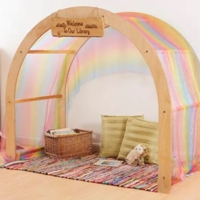 Cabine de leitura infantil com estrutura de madeira, tecido colorido arco-íris e acessórios acolhedores
