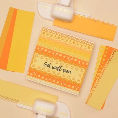 Conjunto de papelaria com papel amarelo e laranja, furadores e cartão com a mensagem Get well soon