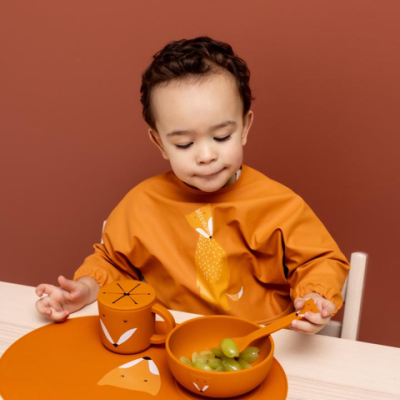Conjunto de copo, tigela e colher laranja com estampa de raposa usado por criança com babete laranja.