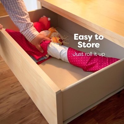 Boneca vermelha e branca a ser guardada numa gaveta de madeira clara com texto 'Easy to Store Just roll it up'