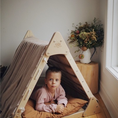 Tenda infantil de madeira com almofada e criança dentro junto a vaso com flores