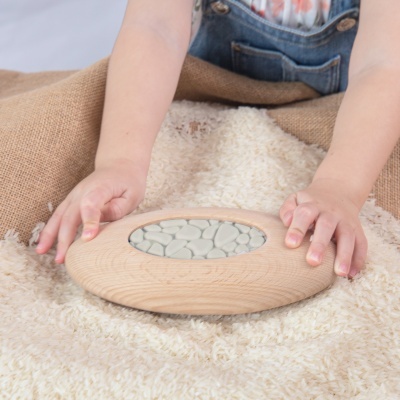 Objeto redondo de madeira clara com centro de pedras brancas sobre tecido felpudo