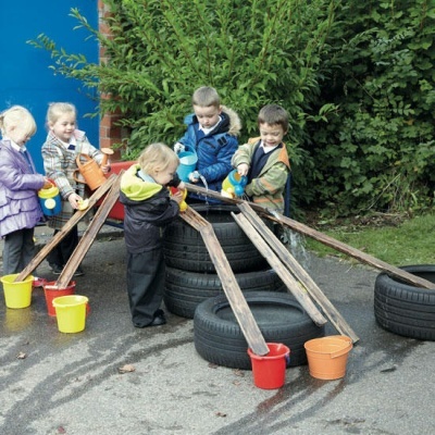 Crianças com baldes coloridos e tubos de madeira apoiados em pneus ao ar livre