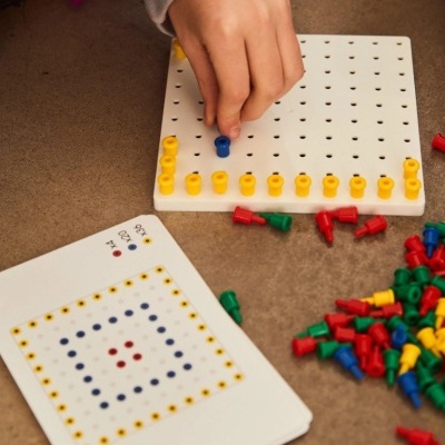 Jogo de lógica com tabuleiro branco perfurado e pinos coloridos