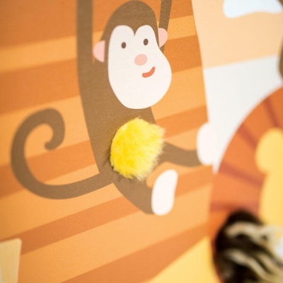 Pormenor de estampa de macaco com pompom amarelo numa superfície listrada em tons de laranja