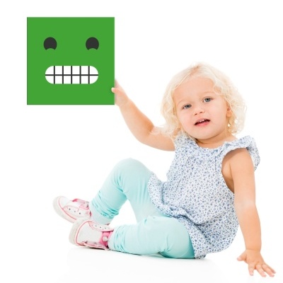 Criança loira sentada a segurar quadrado verde com expressão desenhada