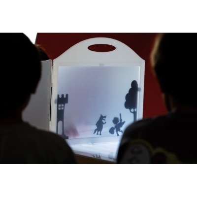 Caixa de sombras branca com figuras recortadas pretas e crianças observando