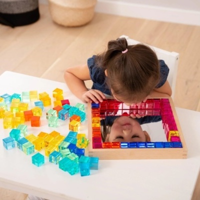 Menina a olhar para um espelho com moldura de blocos coloridos numa mesa branca