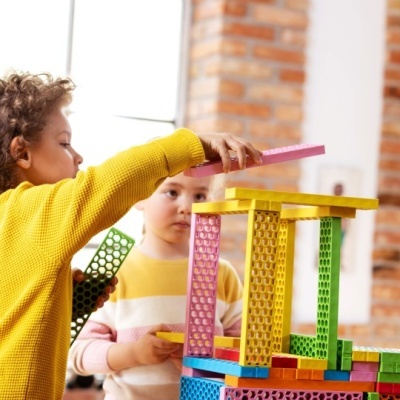 Crianças a brincar com blocos de construção coloridos em sala com parede de tijolos