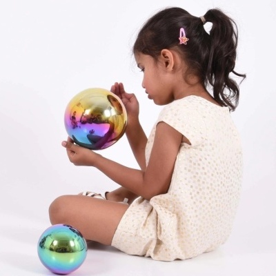 Menina sentada com vestido amarelo claro segurando bola decorativa espelhada colorida