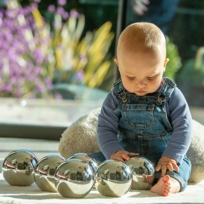 Bebé com jardineira azul a brincar com bolas metálicas refletivas