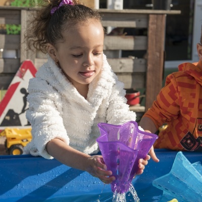 Criança a brincar com brinquedo de água roxo numa mesa azul ao ar livre