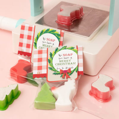 Sabões em forma de árvore e bota com etiquetas de Natal e máquina de embalagem.