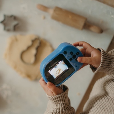 Conjunto de cortantes de bolacha metálicos, massa estendida, rolo de madeira e criança com câmara azul numa cozinha