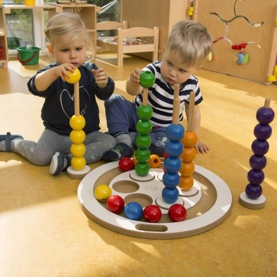 Duas crianças brincam com brinquedo educativo de bolas de madeira coloridas em ambiente interior
