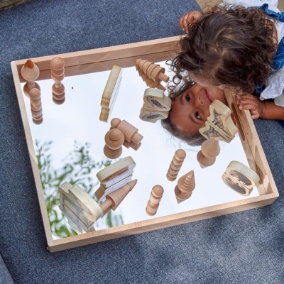 Tabuleiro de madeira com superfície espelhada e peças de madeira esculpidas, criança observando o reflexo.