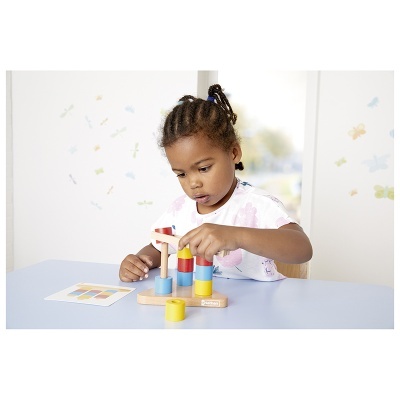 Criança a brincar com brinquedo de madeira colorido em mesa azul, com autocolantes coloridos nas paredes brancas.