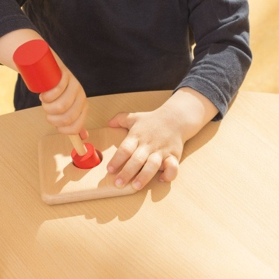 Criança a bater com martelo de madeira vermelho numa base de madeira