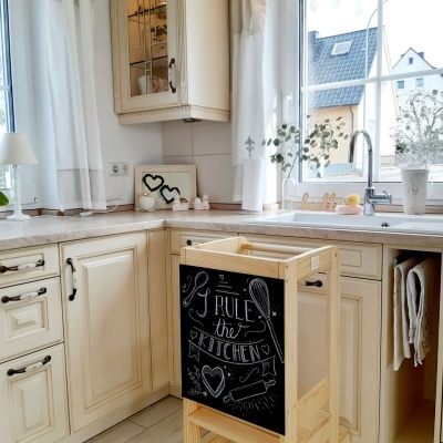 Cadeira alta de madeira clara com quadro-negro escrito I RULE the KITCHEN numa cozinha clara com armários brancos e janela grande