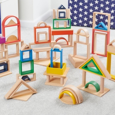 Blocos de construção em madeira coloridos empilhados em diversas formas geométricas sobre chão cinzento