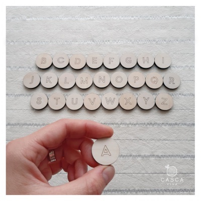 Peças redondas de madeira clara com letras do alfabeto gravadas em superfície branca