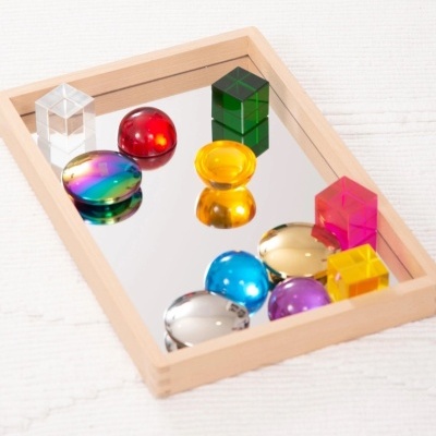 Peças de vidro colorido em diferentes formas numa bandeja de madeira com espelho