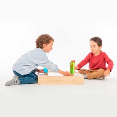 Dois meninos sentados no chão a jogar com brinquedo de madeira com copos coloridos.