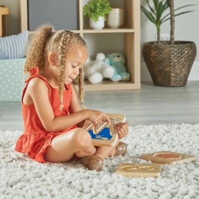Menina sentada numa carpete branca felpuda a brincar com brinquedo educativo de madeira