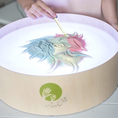 Mesa de areia multicolorida em tabuleiro redondo de madeira clara com marca SonElu