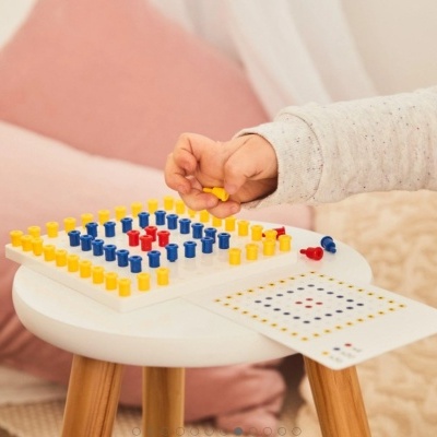 Jogo de tabuleiro com peças coloridas e mão de criança a jogar numa mesa pequena