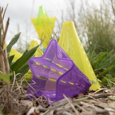 Cones de treino de plástico com formatos estrela e cónico em roxo translúcido e amarelo sobre relva