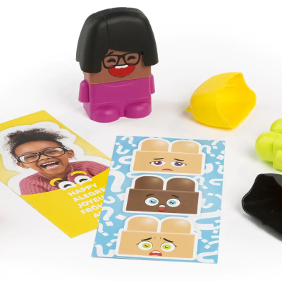 Boneco de plástico cor de pele, roupa rosa, cartões com rostos expressivos e cartão com criança sorridente