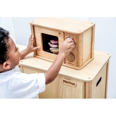 Criança a usar micro-ondas de madeira da PlanToys sobre móvel de madeira.