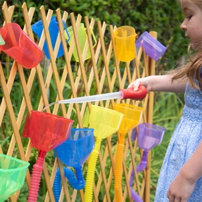Menina a regar copos coloridos de plástico pendurados numa cerca de madeira num jardim