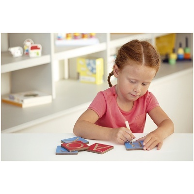 Criança a escrever num tabuleiro com letras em mesa branca